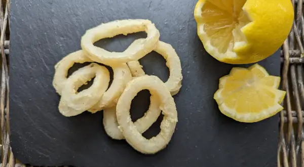 Anneaux de calamar à l'andalouse dorés et croustillants, servis avec un quartier de citron sur une ardoise.