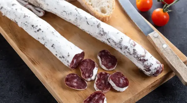 Deux saucissons secs, dont un tranché, sur une planche en bois avec du pain et des tomates cerises. Un délice de saucisson au genévrier.