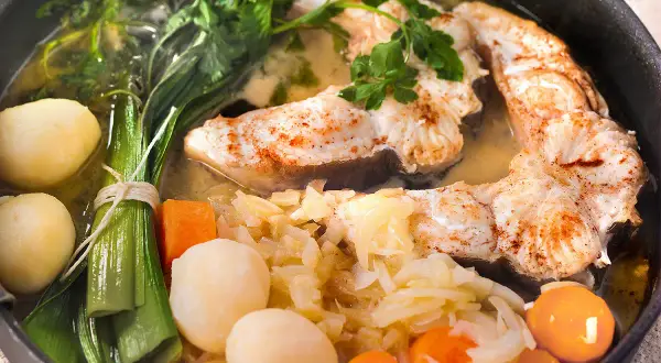 Un plat appétissant de daube de congre, avec des morceaux de poisson tendres, des pommes de terre, des carottes et des poireaux, le tout mijoté dans un bouillon savoureux.