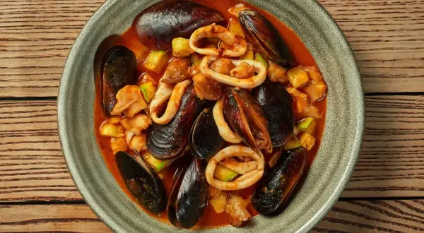 Zarzuela la vraie recette espagnole : un plat de fruits de mer savoureux avec des moules, des calamars et des légumes dans une sauce rouge.