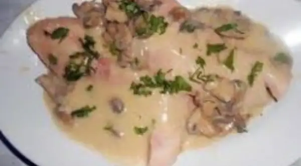 Délicieux jambon braisé au cidre, nappé d'une sauce crémeuse aux champignons et parsemé de persil frais. Un plat réconfortant.