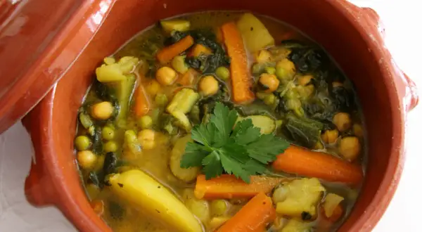 Un savoureux tajine végétarien aux carottes, pois chiches, pommes de terre et courgettes, garni de persil frais.