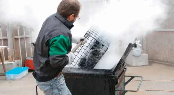 Un homme en tenue de travail manipule une grille au-dessus d'un récipient fumant, peut-être pour un gigot bitume.