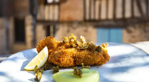 Un plat de ris de veau meunière croustillant, garni de câpres et servi avec un quartier de citron et une sauce verte.
