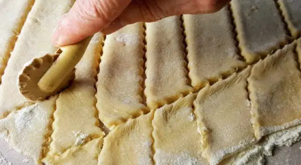Main d'une personne utilisant une roulette pour découper une pâte à gâteau en losanges.
