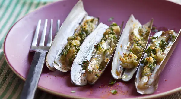 Couteaux cuisinés, une recette de chapeau chinois coquillage, servis sur une assiette rose avec une fourchette.