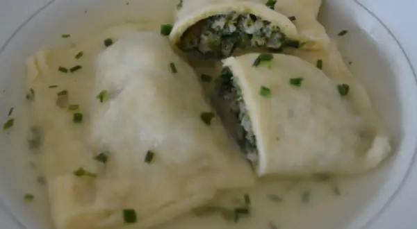 Trois maultaschen à la poêle, généreusement garnies de légumes verts et de viande, baignent dans un bouillon clair, parsemé de ciboule fraîche.