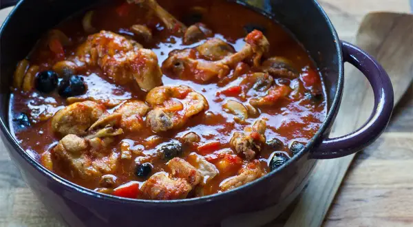 Un plat mijoté de râble de lapin à la provençale, avec des olives noires et des champignons, dans une cocotte en fonte.