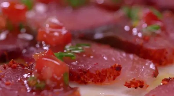Carpaccio de bonite, fines tranches de poisson cru garnies de dés de tomates rouges et d'herbes vertes, assaisonné d'épices.