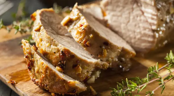 Tranches de porc rôti, parfaites pour le temps de cuisson cochon de lait au barbecue. Garnies d'herbes fraîches sur une planche en bois.