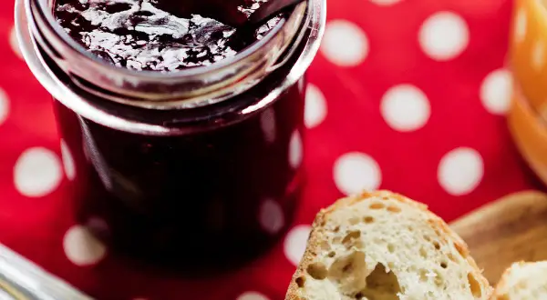Un pot de confiture sombre, peut-être d'origine confiture de vieux garçon, sur une nappe à pois rouges. Du pain frais est prêt à être tartiné.