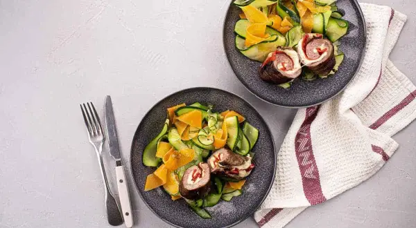 Deux assiettes de involtini de boeuf avec une salade de courgettes et carottes en rubans. Un repas léger et coloré.