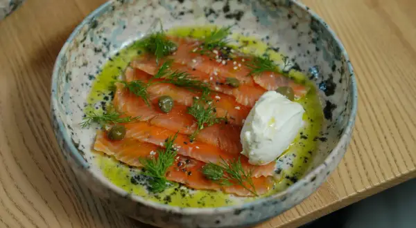 Saumon gravlax maison, fines tranches de poisson cru mariné, garnies d'aneth, de câpres et d'une quenelle de crème fraîche.
