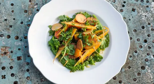 Salade colorée de carottes confites, parsemée d'herbes fraîches et de fines lamelles de radis, sur une assiette blanche.