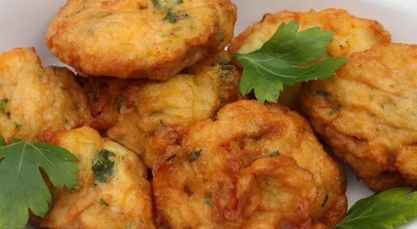 Des beignets dorés et croustillants, comme les farinettes de grand-mère, garnis d'herbes fraîches, dans un plat blanc.