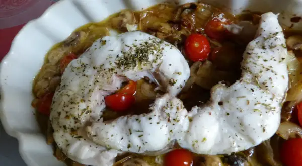 Filet de congre au four, tendre et savoureux, servi avec des tomates cerises et des champignons dans un plat blanc.