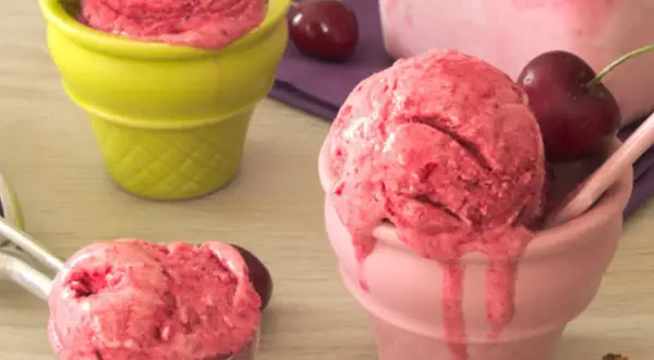 Trois coupes colorées servent une délicieuse recette sorbet cerise, avec des cerises fraîches et une cuillère à glace.