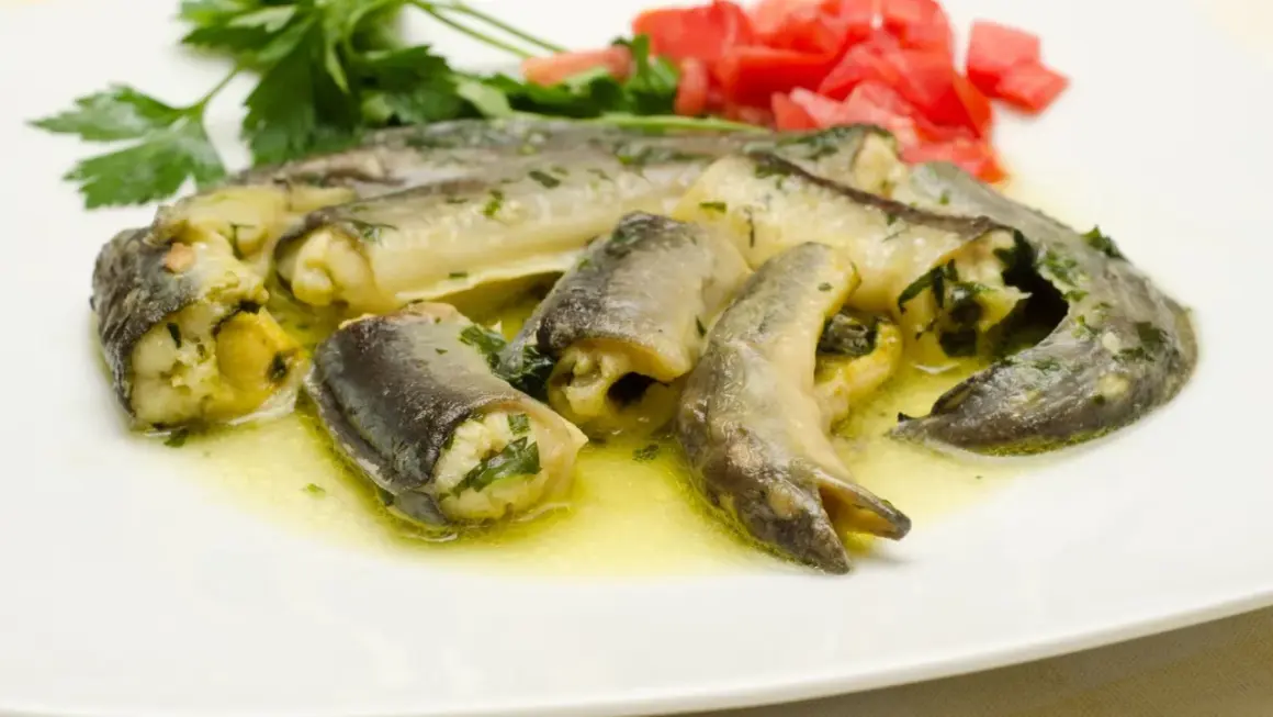 Délicieux morceaux d'anguille roulée, baignant dans une sauce dorée, parfaits pour apprendre comment préparer une anguille. Garniture de persil et tomates.
