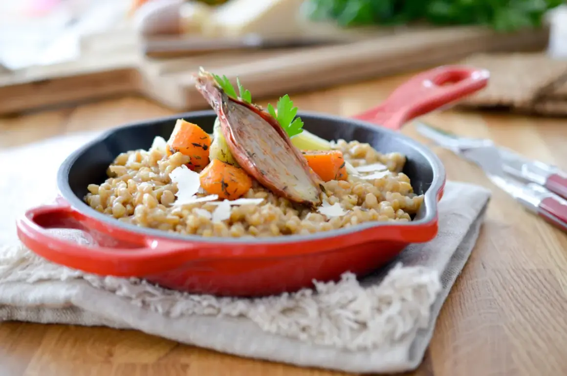Un savoureux risotto d'épeautre garni de carottes rôties et d'une échalote confite, servi dans une cocotte rouge.
