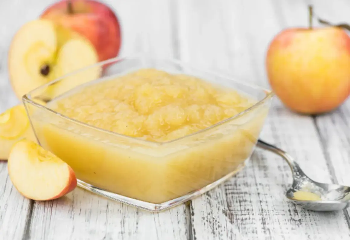 Un bol de compote pommes poires maison, avec des pommes fraîches coupées en arrière-plan.