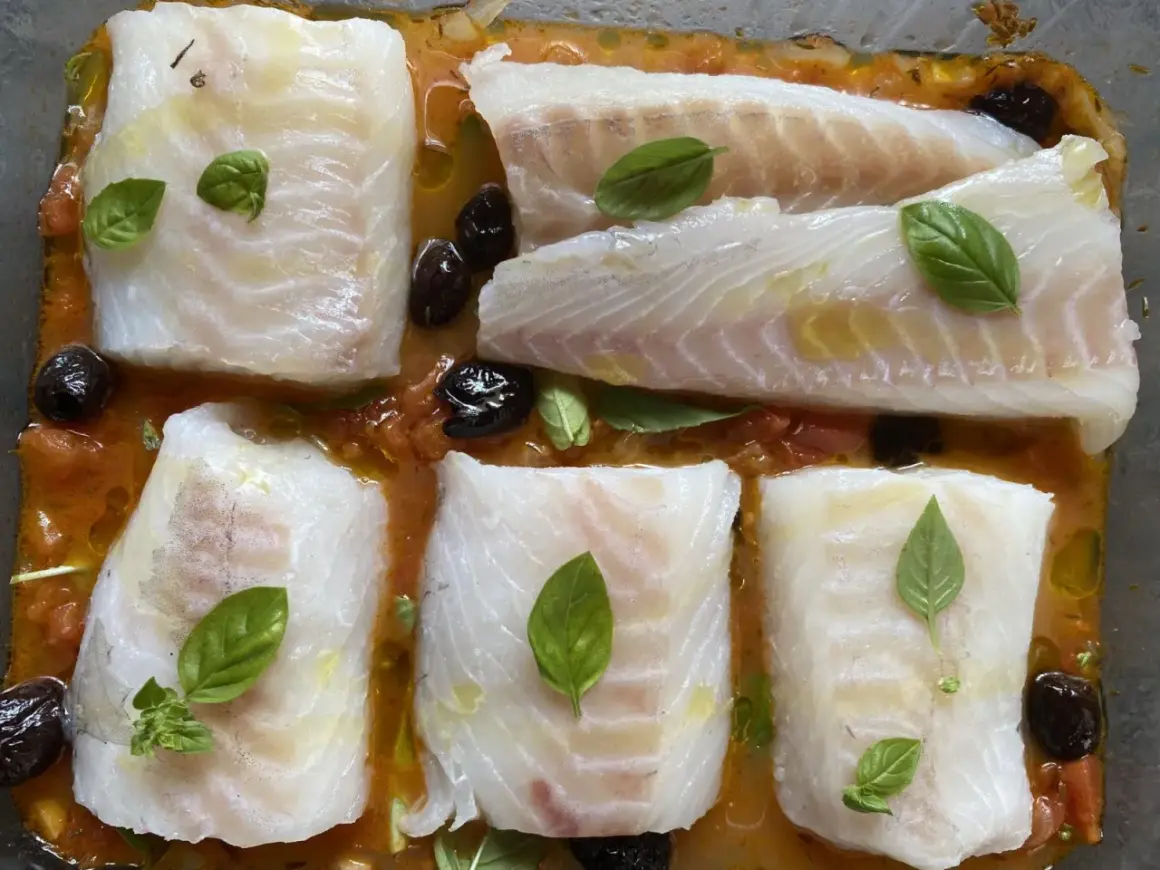 Cinq pavés de dos de cabillaud à la provençale au four, baignant dans une sauce tomate et olives, ornés de feuilles de basilic frais.