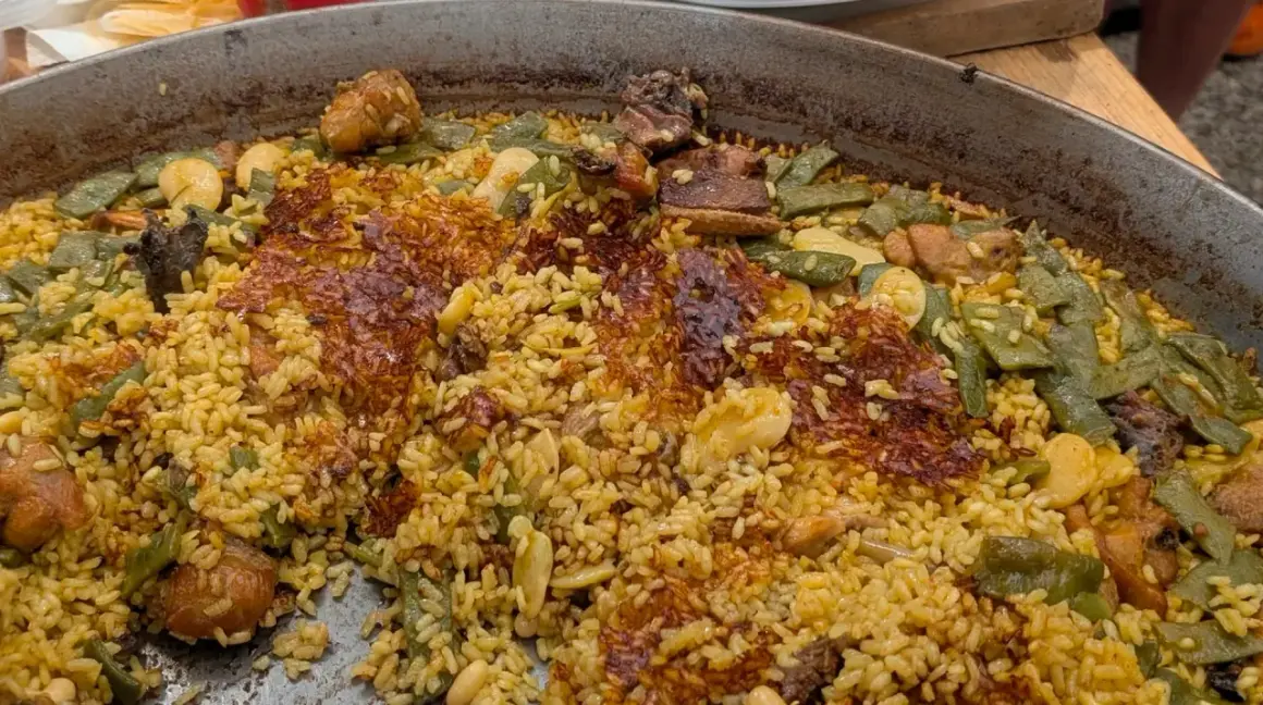 Gros plan sur une paella au feu de bois, avec du riz doré, des haricots verts, des morceaux de viande et une croûte croustillante.