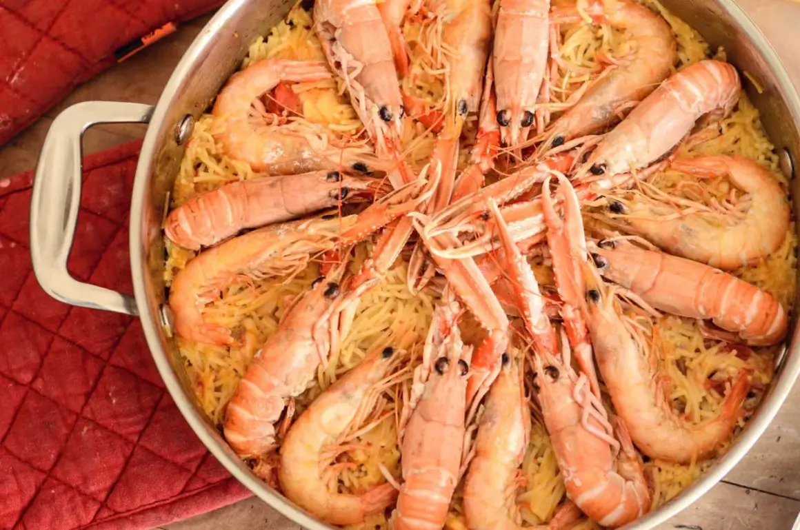 Un plat de fideuà catalana, avec des pâtes fines et des crevettes roses généreuses, prêt à être dégusté.