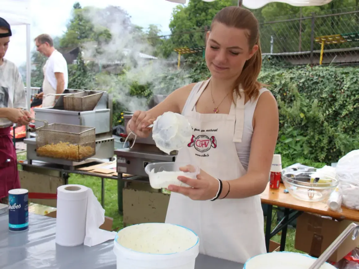 Une jeune femme prépare une recette chique de sauce crémeuse. Derrière elle, des frites dorent dans une friteuse.