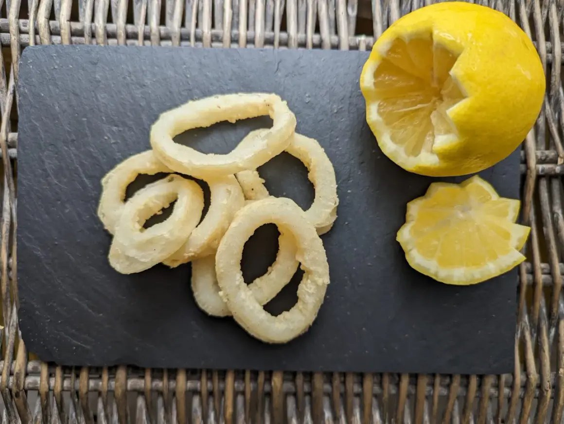 Anneaux de calamar à l'andalouse dorés et croustillants, servis avec un quartier de citron sur une ardoise.