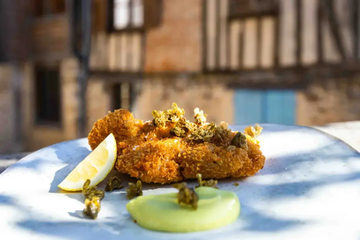 Un plat de ris de veau meunière croustillant, garni de câpres et servi avec un quartier de citron et une sauce verte.