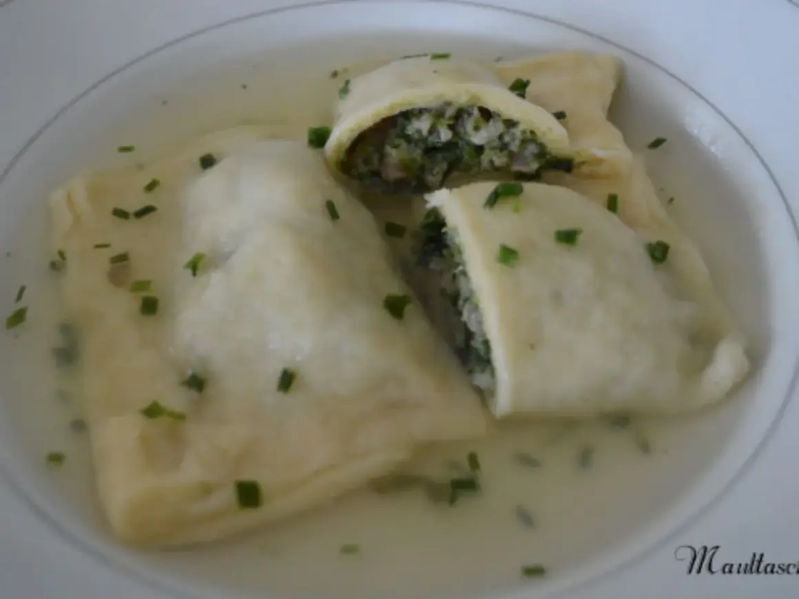 Trois maultaschen à la poêle, généreusement garnies de légumes verts et de viande, baignent dans un bouillon clair, parsemé de ciboule fraîche.
