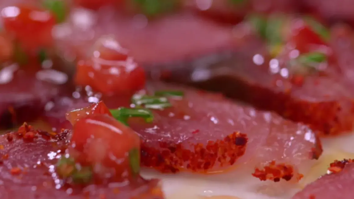 Carpaccio de bonite, fines tranches de poisson cru garnies de dés de tomates rouges et d'herbes vertes, assaisonné d'épices.