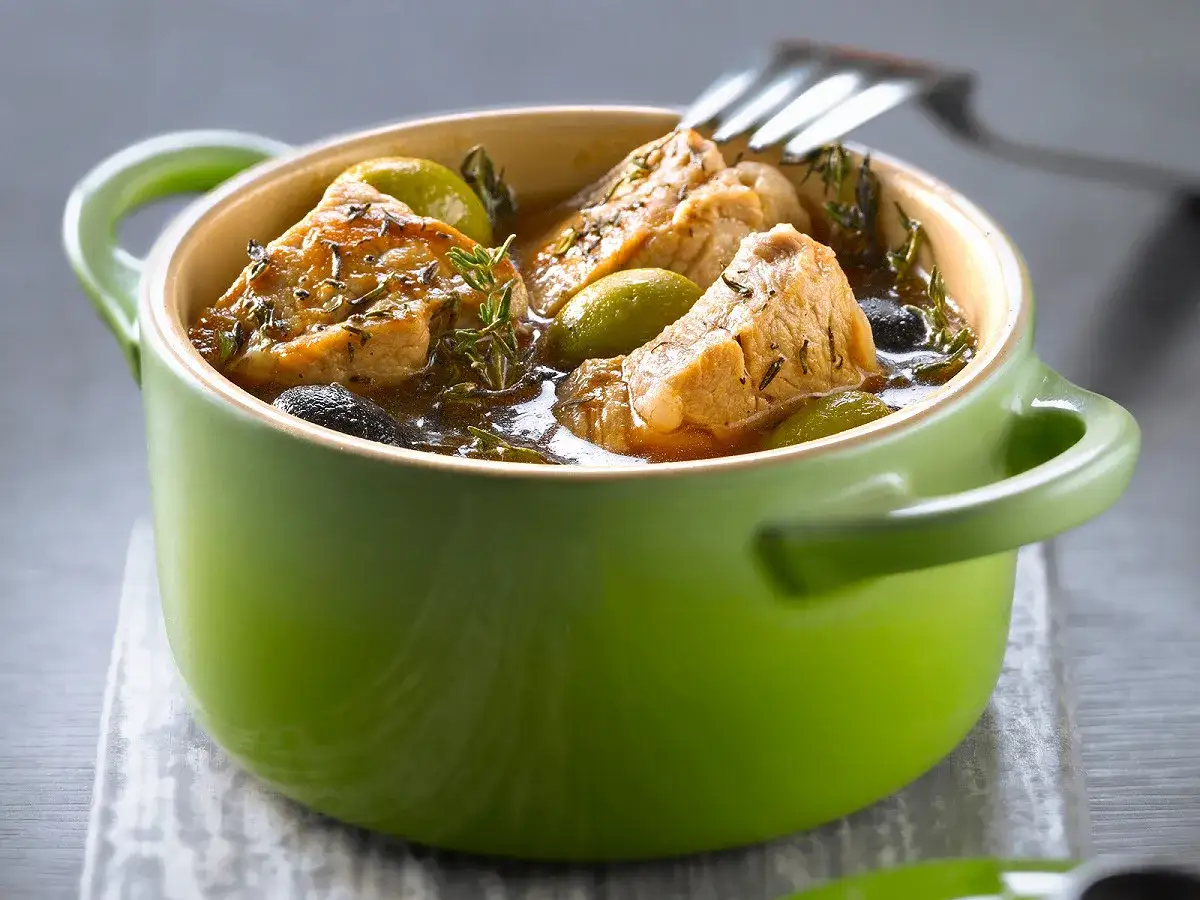 Un savoureux ragout corse mijote dans une cocotte verte, avec des morceaux de viande, des olives et des herbes aromatiques.