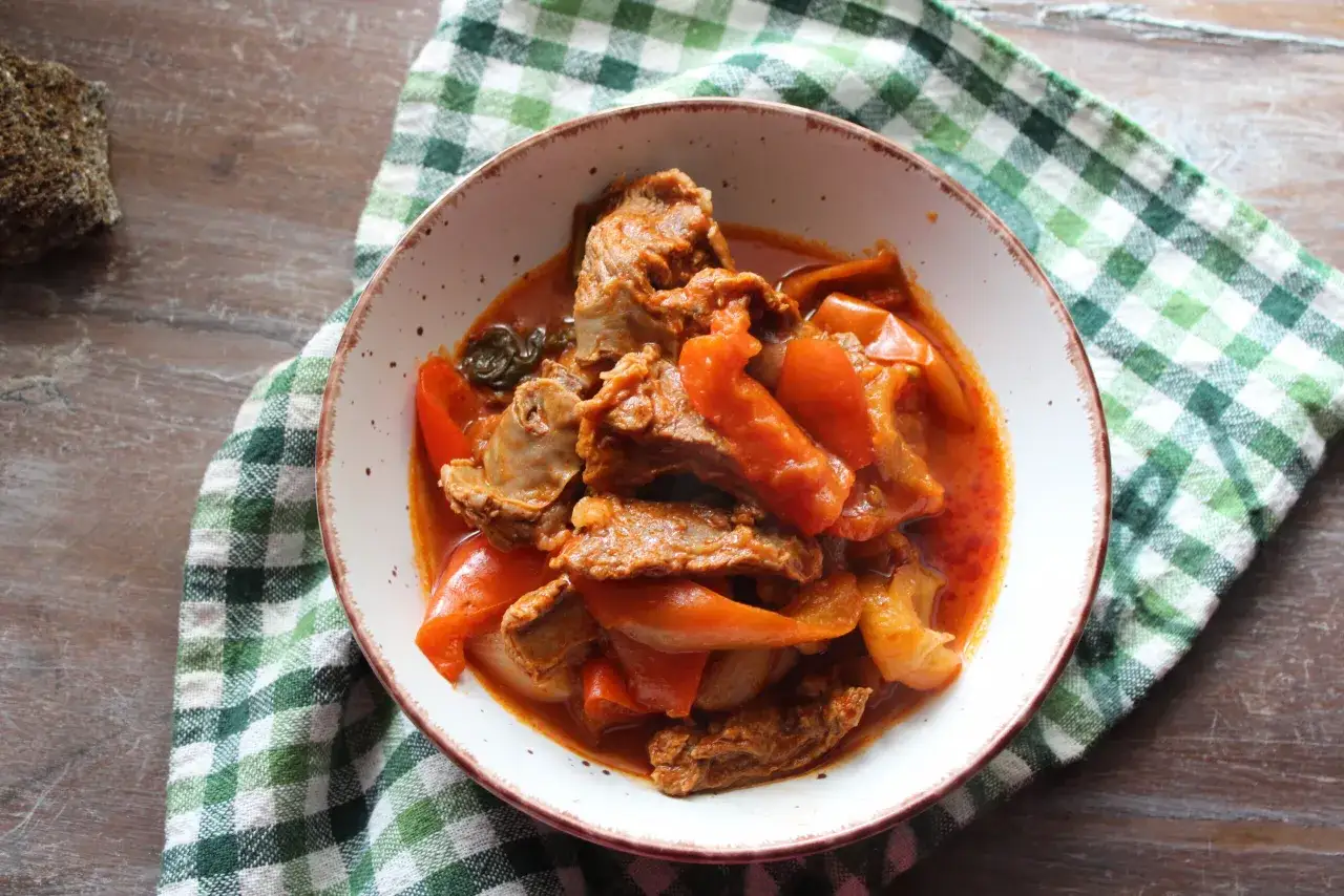 Un plat de chanfana portugal, un ragoût de chèvre mijoté, servi dans un bol avec des morceaux de poivrons rouges et une sauce savoureuse.