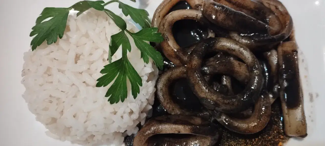 Calamar à l'encre, une recette espagnole savoureuse, servi avec du riz blanc et une touche de persil.