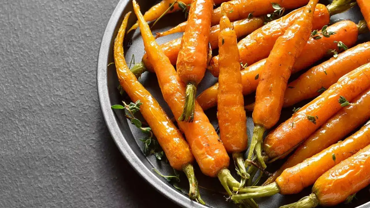 Carottes confites brillantes et caramélisées, parsemées de thym frais, dans un plat sombre. Un délice visuel.
