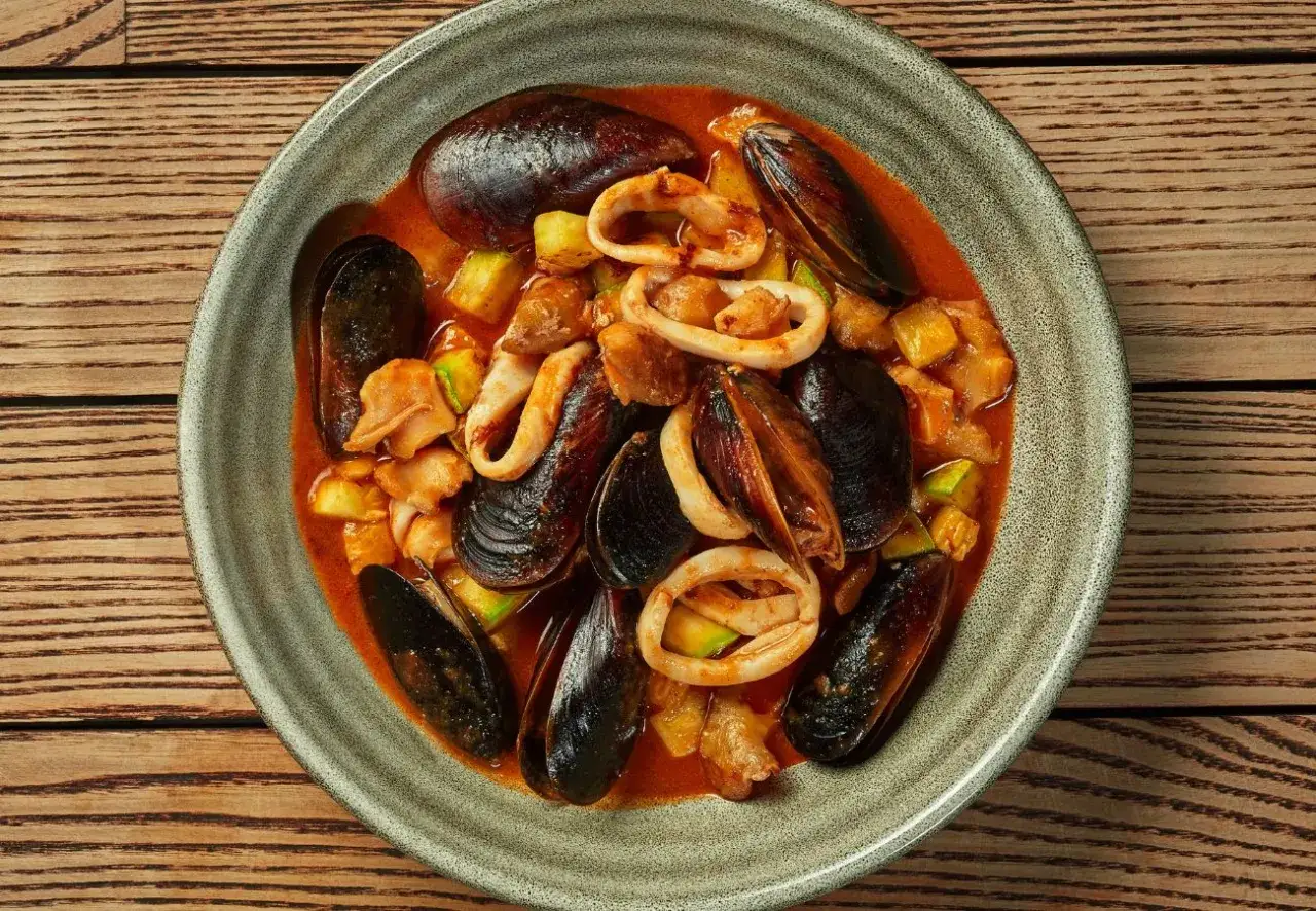 Zarzuela la vraie recette espagnole : un plat de fruits de mer savoureux avec des moules, des calamars et des légumes dans une sauce rouge.
