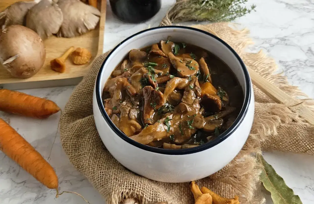 Un savoureux bourguignon végétarien aux champignons, servi dans un bol blanc, avec des carottes et des herbes fraîches.