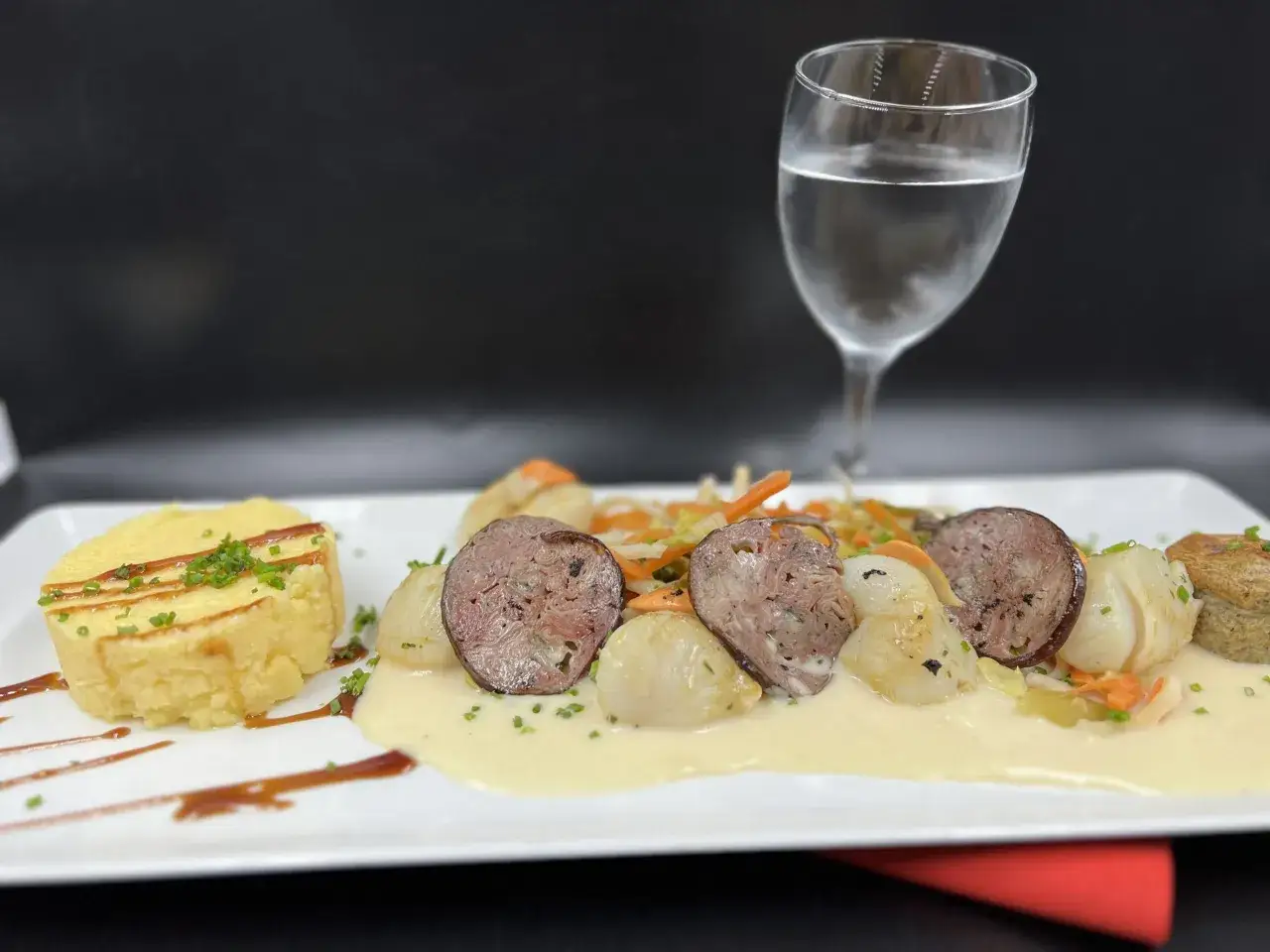 Une assiette gourmande avec une andouille chaude du Nord, des Saint-Jacques poêlées, un flan de légumes et une sauce crémeuse.
