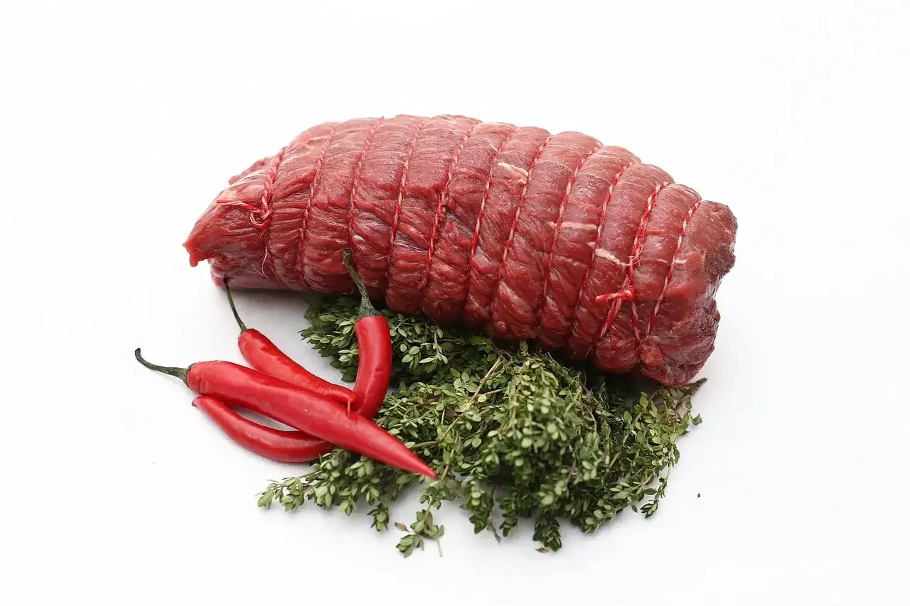 Un rond de tranche de bœuf, prêt pour une recette savoureuse, accompagné de piments rouges et de thym frais.