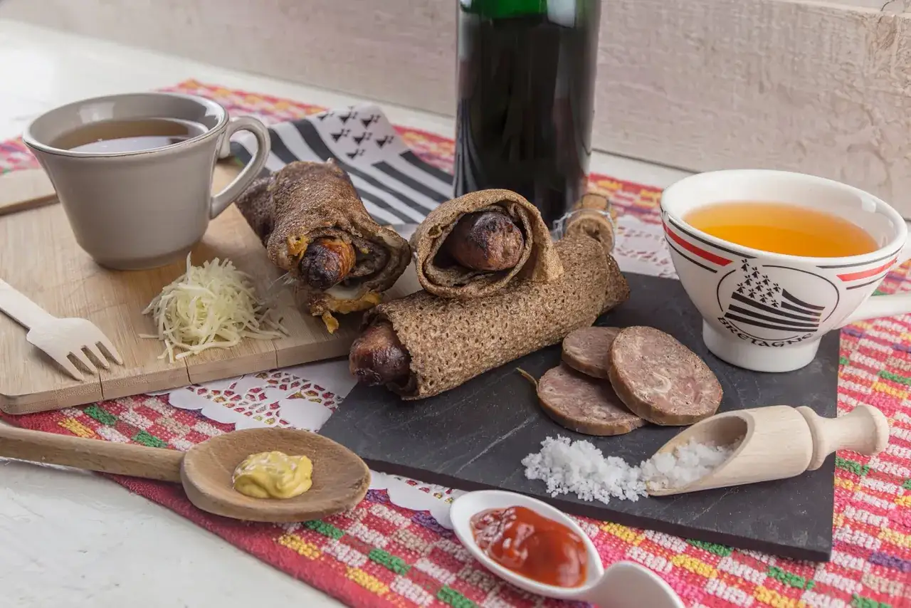 Galettes de sarrasin garnies de saucisses, une spécialité bretonne viande, accompagnées de moutarde, ketchup et d'une tasse de cidre.