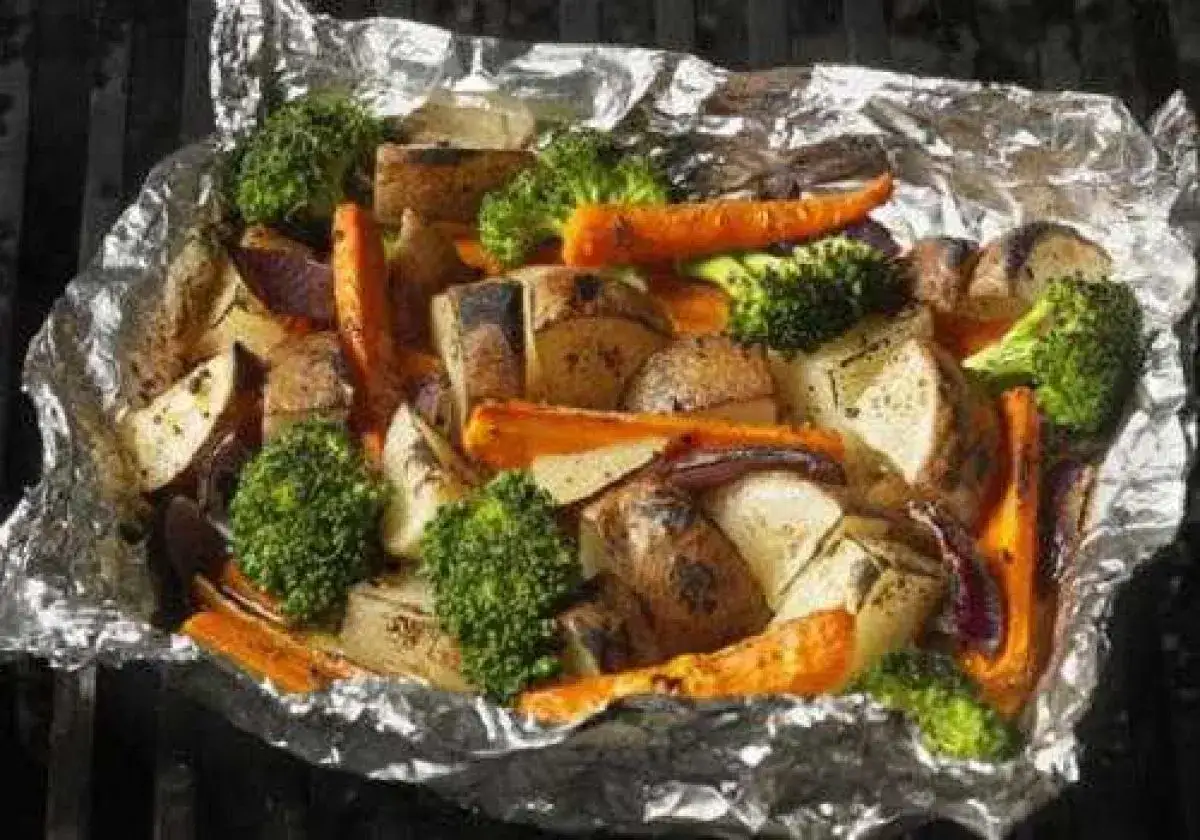 Légumes variés (carottes, pommes de terre, brocolis, oignons rouges) cuits en papillote sur un barbecue.