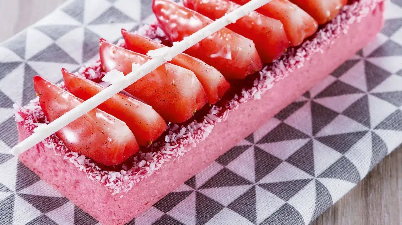 Un délicieux gâteau zéphyr rose, garni de fraises fraîches et de noix de coco râpée, sur une serviette à motifs géométriques.