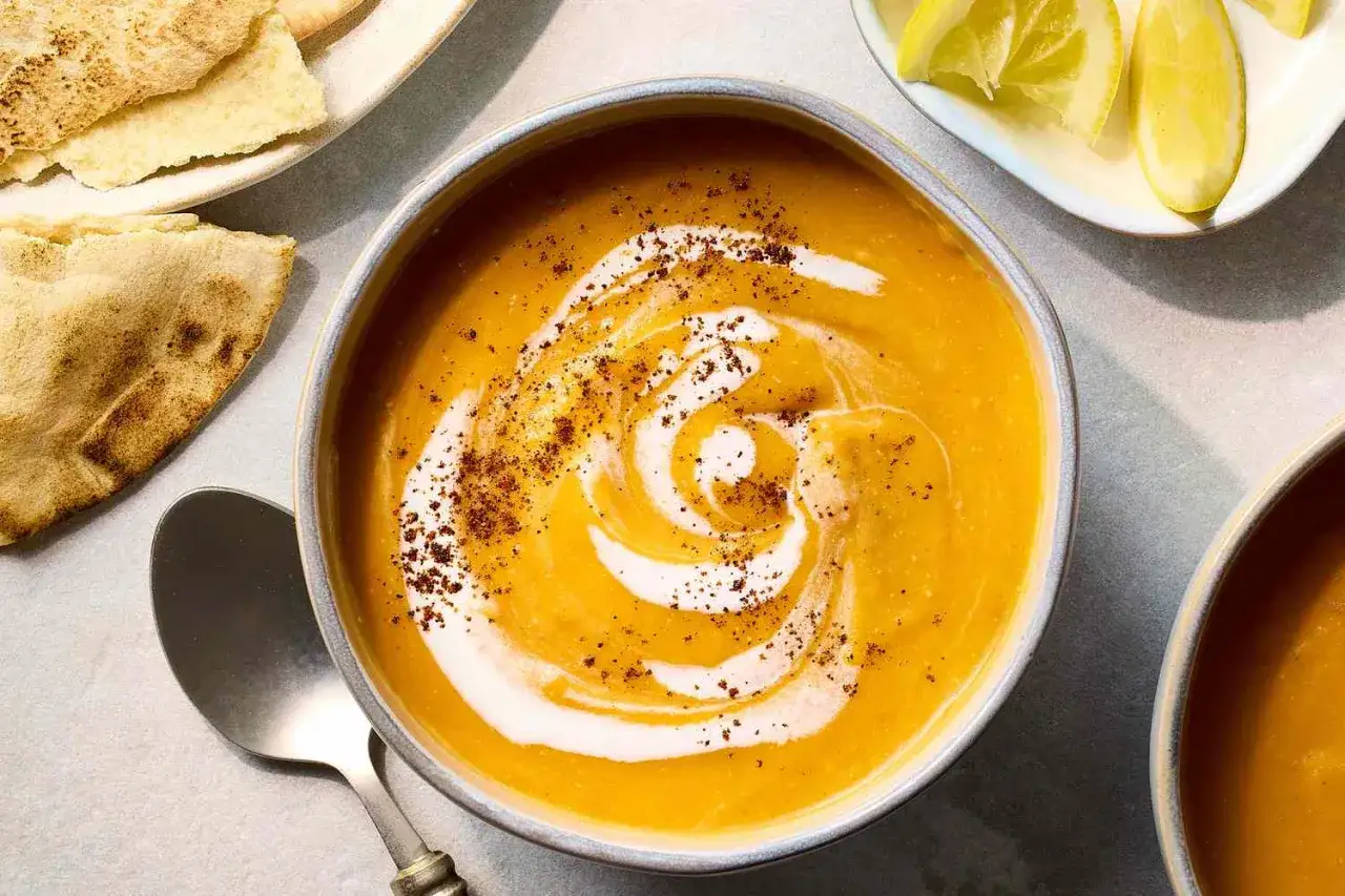 Une soupe égyptienne onctueuse, garnie de crème et d'épices, servie avec du pain pita et des quartiers de citron.