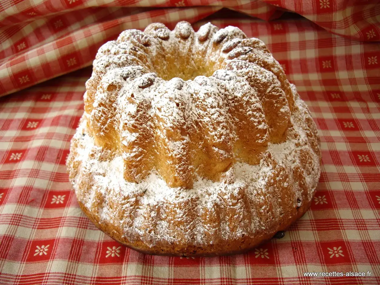 Un kougelhopf, recette kougelhopf de grand-m&egrave;re alsacienne, saupoudr&eacute; de sucre glace, sur une nappe &agrave; carreaux rouges et blancs.