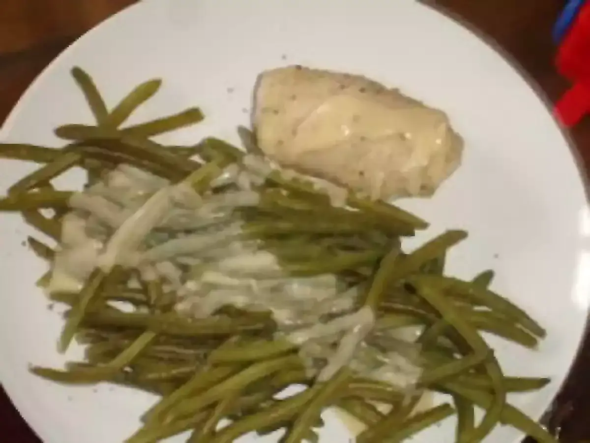Un plat de haricots verts en sauce blanche, avec un morceau de poulet nappé de sauce crémeuse. Un délice simple et savoureux.