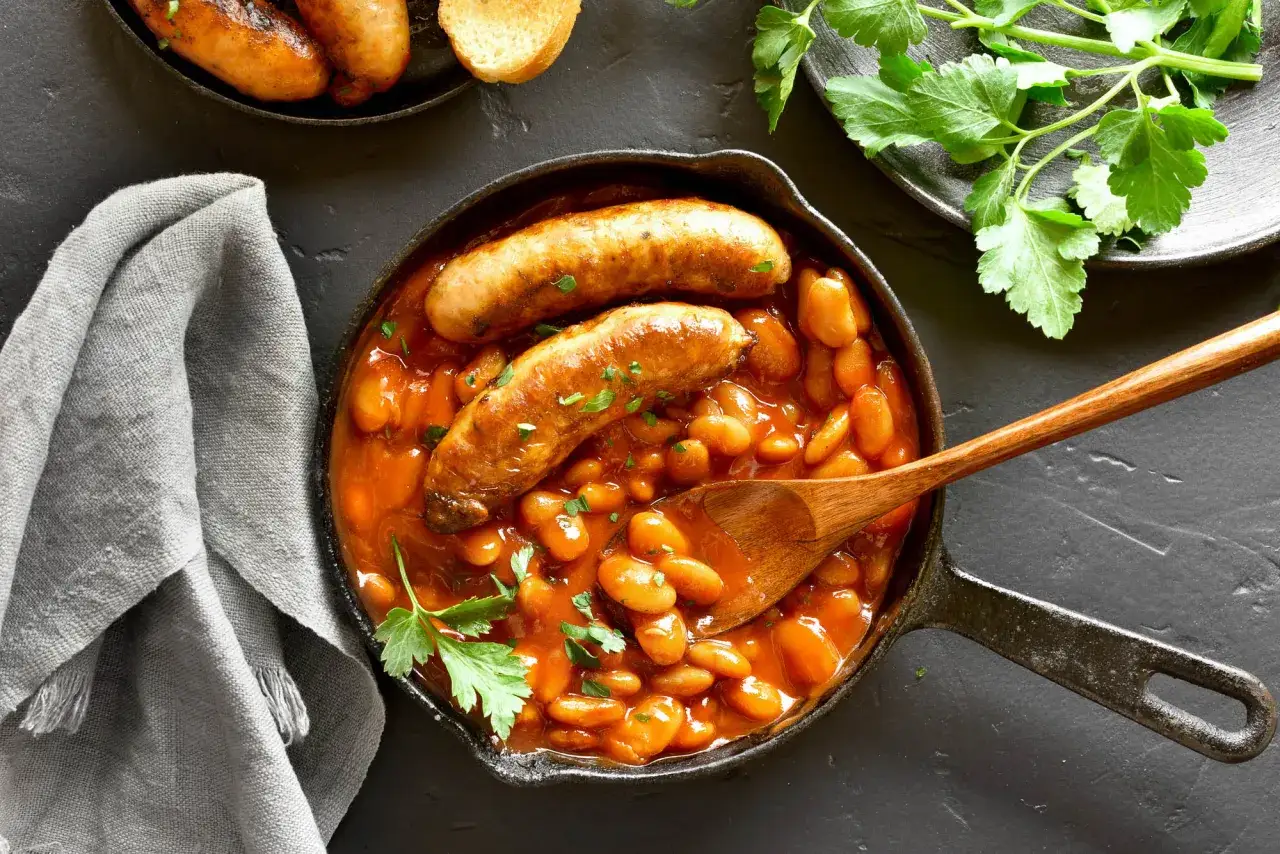 Saucisses catalanes dans une poêle avec des haricots blancs en sauce tomate. Une recette savoureuse et réconfortante.