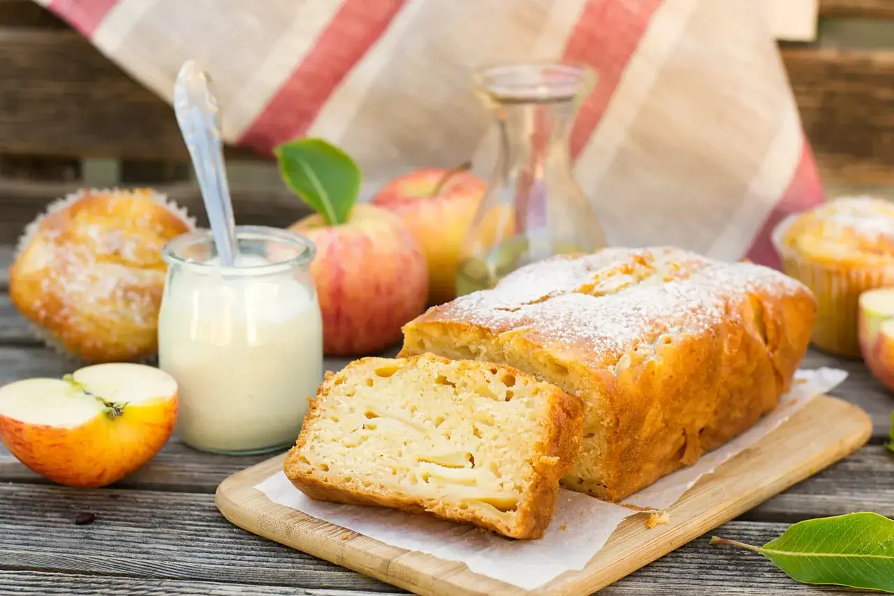 Un délicieux gâteau d'Ève d'origine, parsemé de sucre glace, accompagné de pommes et d'une crème onctueuse.