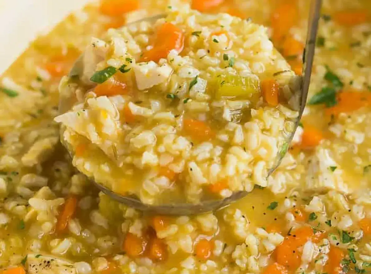 Une louche remplit de soupe au riz grand-mère, avec des morceaux de poulet, carottes et céleri. Un plat réconfortant.