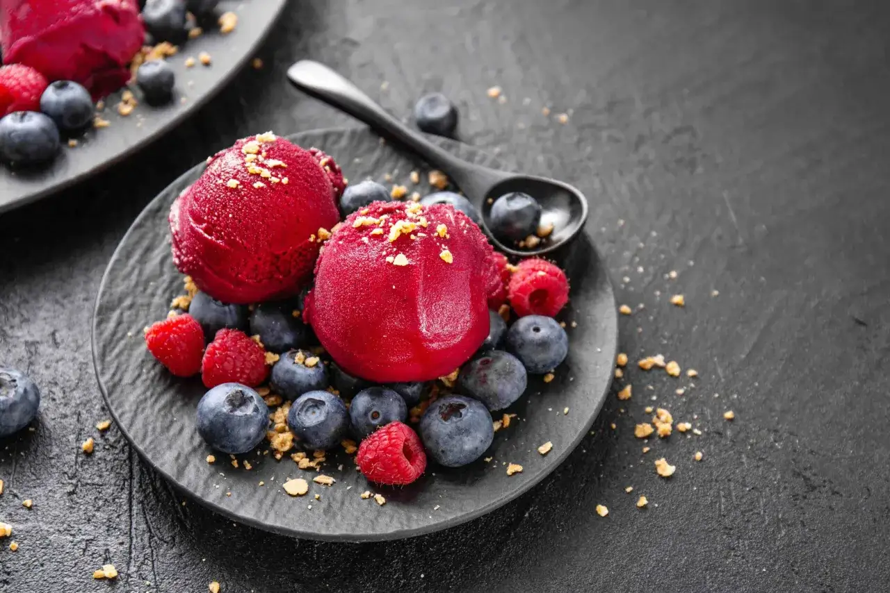 Glace rouge vif aux fruits congelés et yaourt, parsemée de fruits frais et de miettes croustillantes. Une recette simple et délicieuse.
